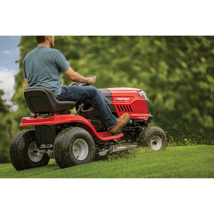 Person riding a red riding lawn mower in a grassy area